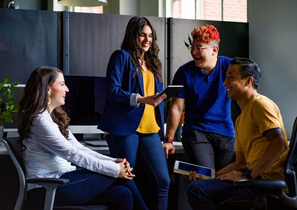 Four people gathered together, laughing while looking at their tablets.
